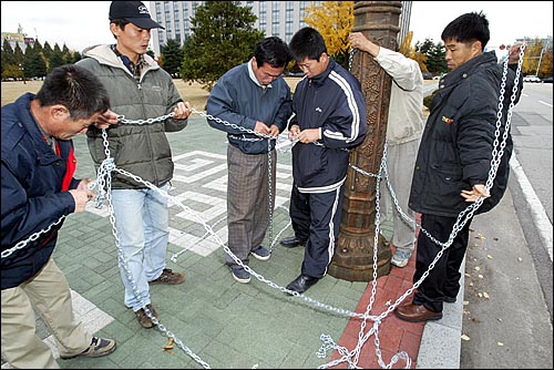 가로등 기둥과 자신의 몸을 쇠사슬로 두른 뒤 자물쇠를 채우고 있다. 